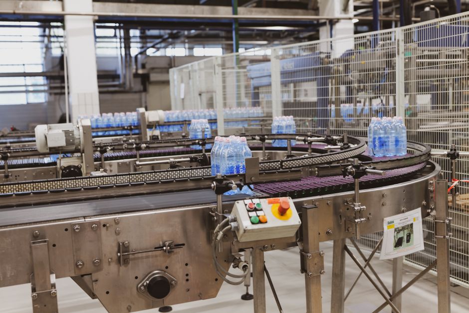 Exportação Agronegócio — Water bottles being processed on an automated conveyor in a modern factory setting.